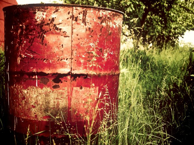 Rusty red barrel in overgrown grass
