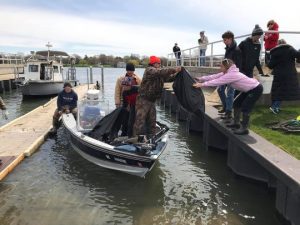 Man on boat handing bag of trash to a person on shore 